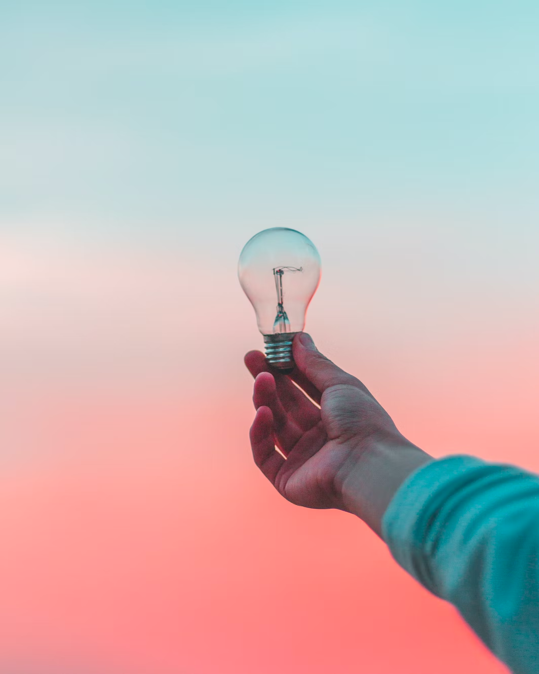 a person's hand holding a lightbulb with a sunset in the background